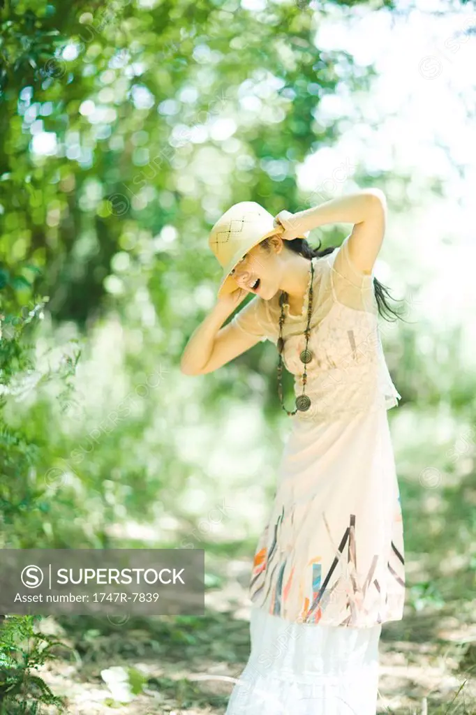 Young woman standing outdoors, putting on sun hat
