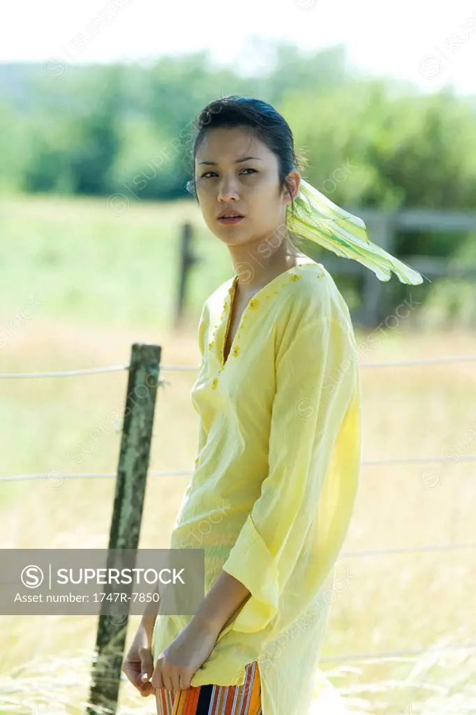 Young woman standing by rural fence