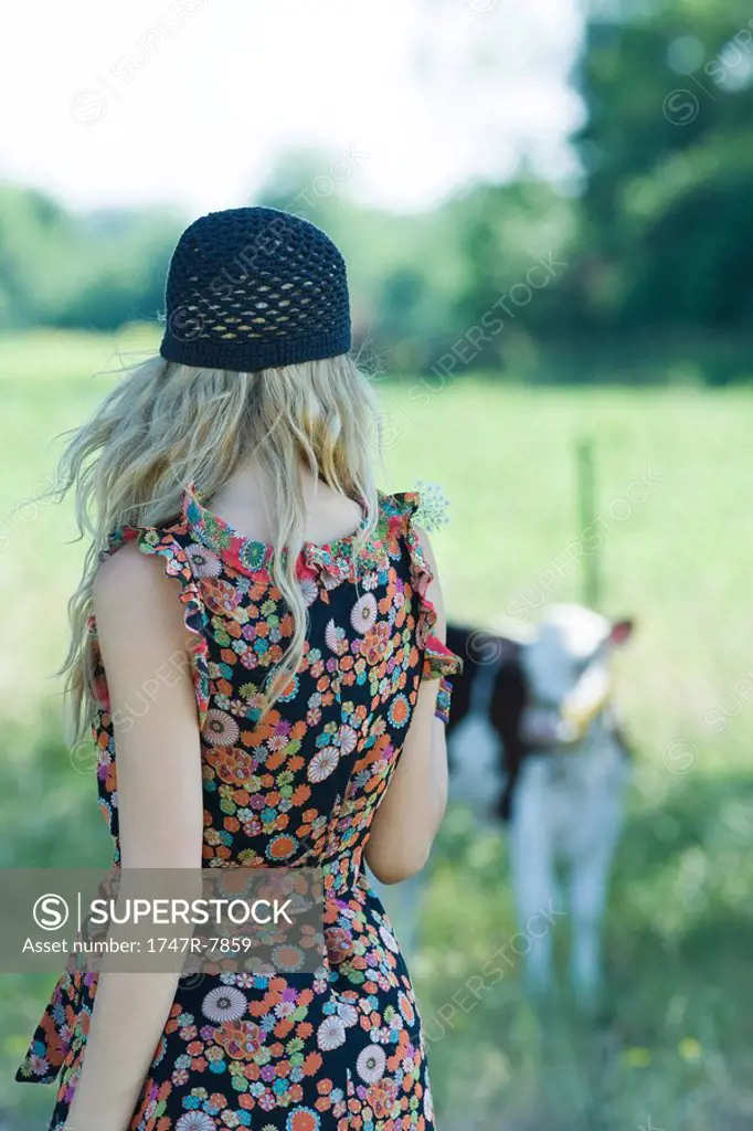 Young woman in sundress walking toward cow, rear view