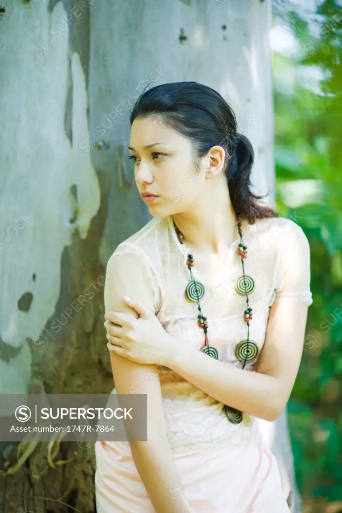 Young woman leaning against tree, looking away