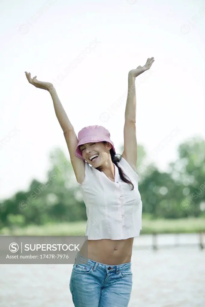 Woman standing with arms raised, showing bare midriff, smiling at camera