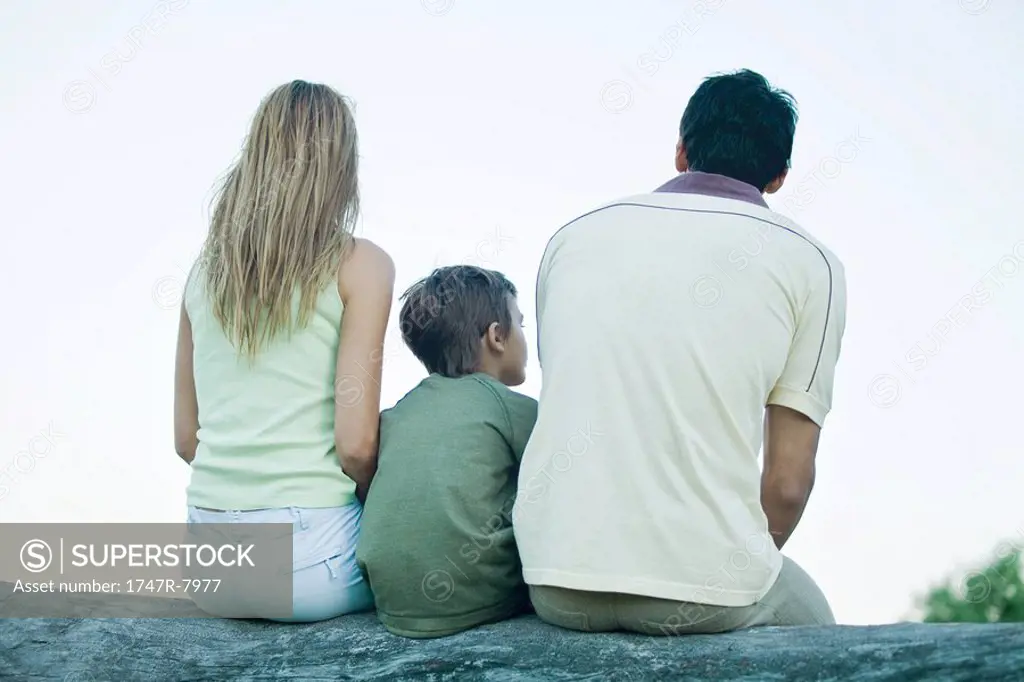 Boy with parents, sitting on log, rear view