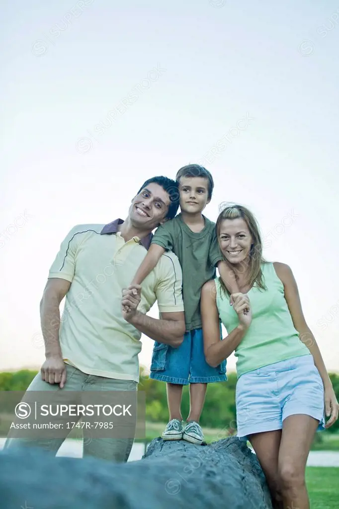 Boy standing on log, between parents
