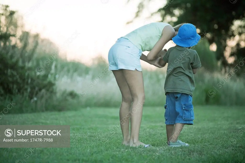 Mother and son standing on lawn, woman bending over to talk to boy