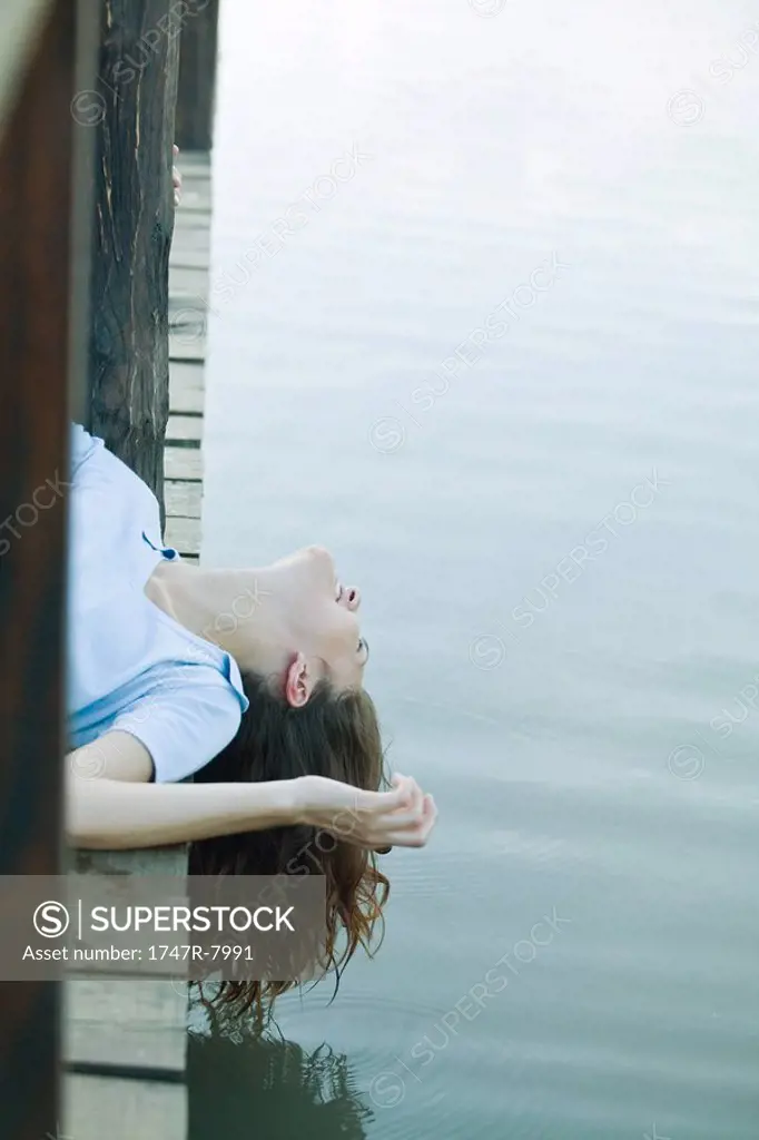 Woman lying on dock, dangling head off edge