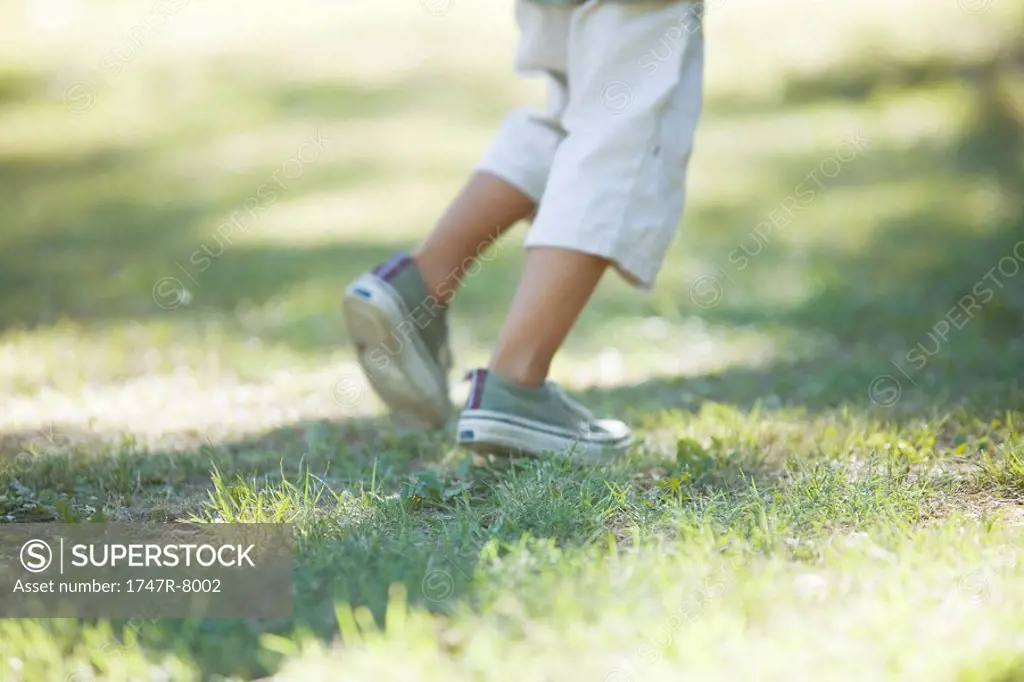 Boy walking across grass, low section