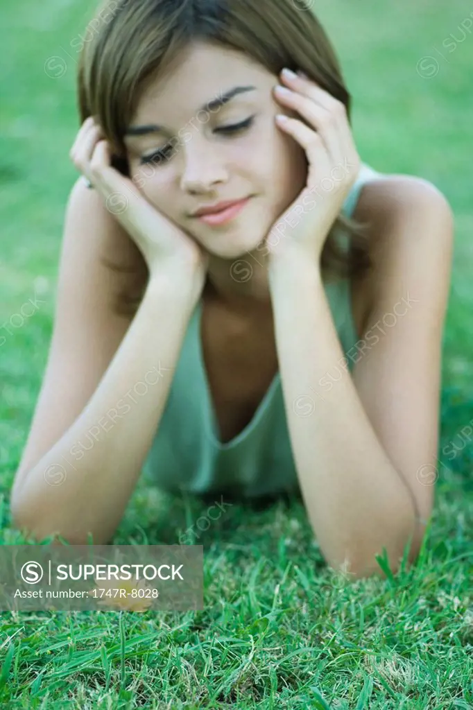 Young woman lying on grass looking down at single yellow flower