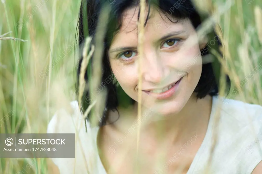 Woman smiling at camera, blurred vegetation in foreground, head and shoulders
