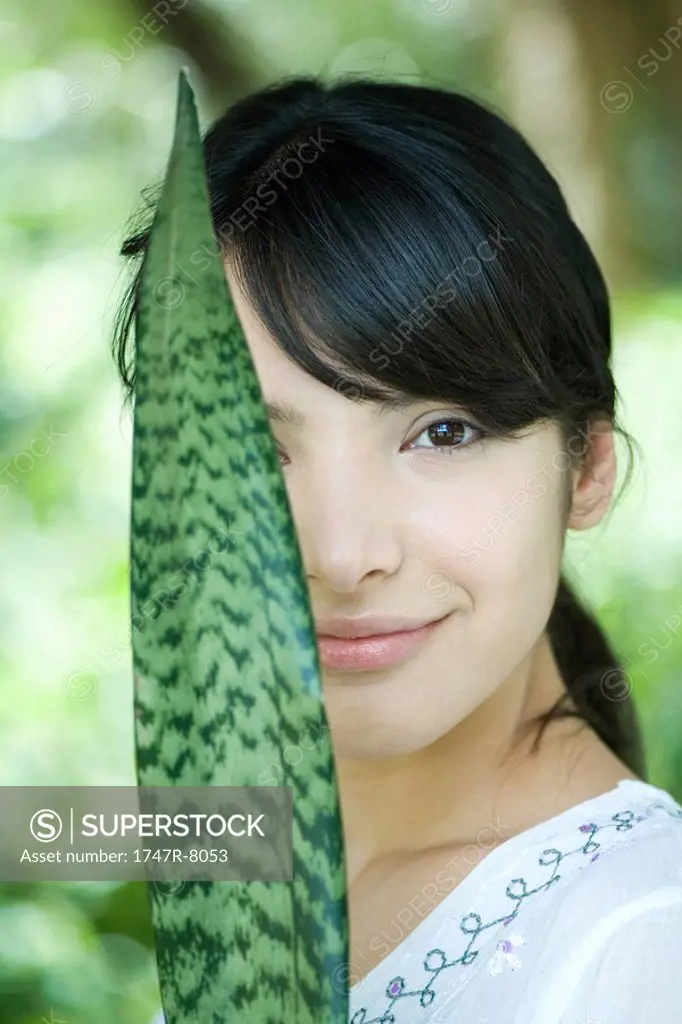 Woman holding up snake plant leaf in front of half of face, portrait