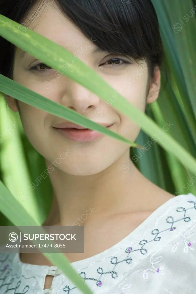 Woman smiling at camera through foliage, portrait