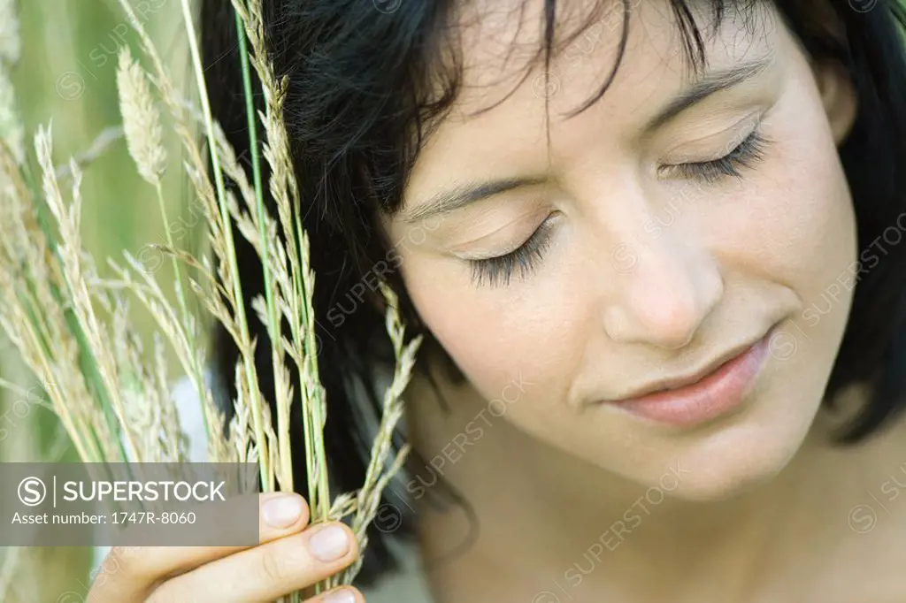 Woman holding handful of vegetation up to face, eyes closed, close-up