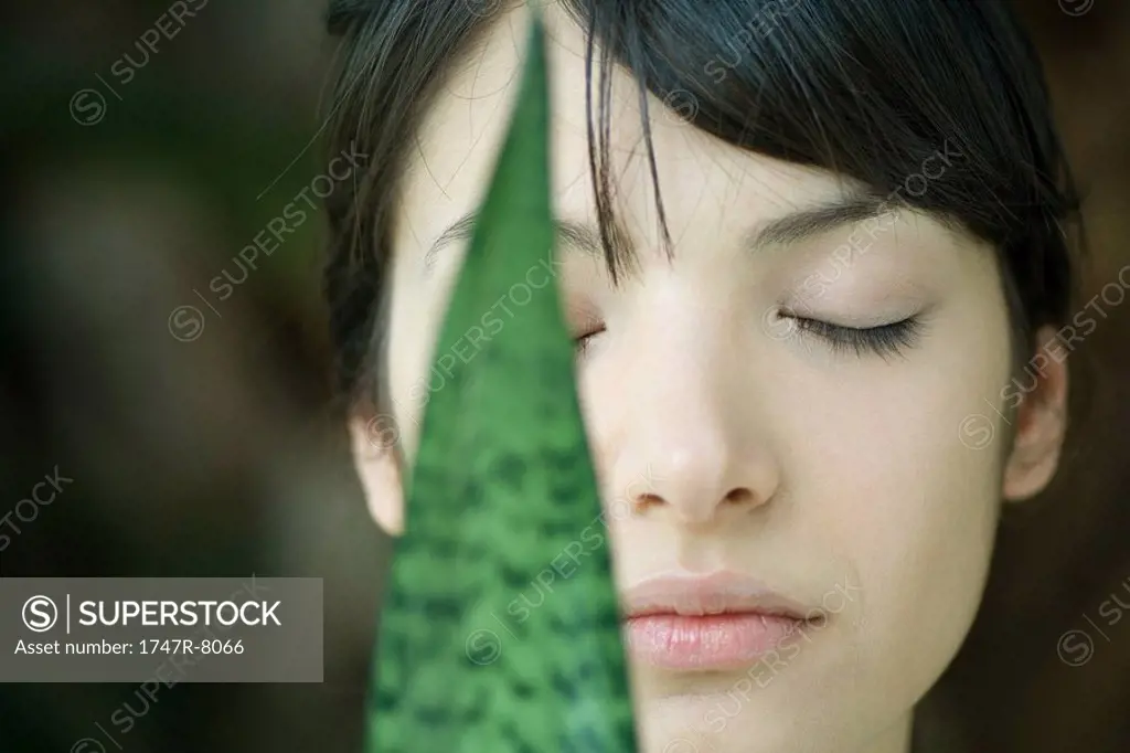 Snake plant leaf in front of woman´s face, eyes closed, close-up