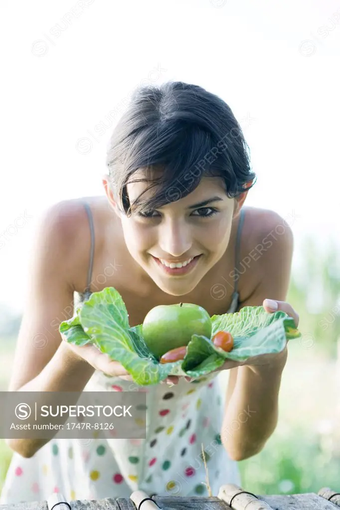 Young woman holding up fresh produce, smiling at camera