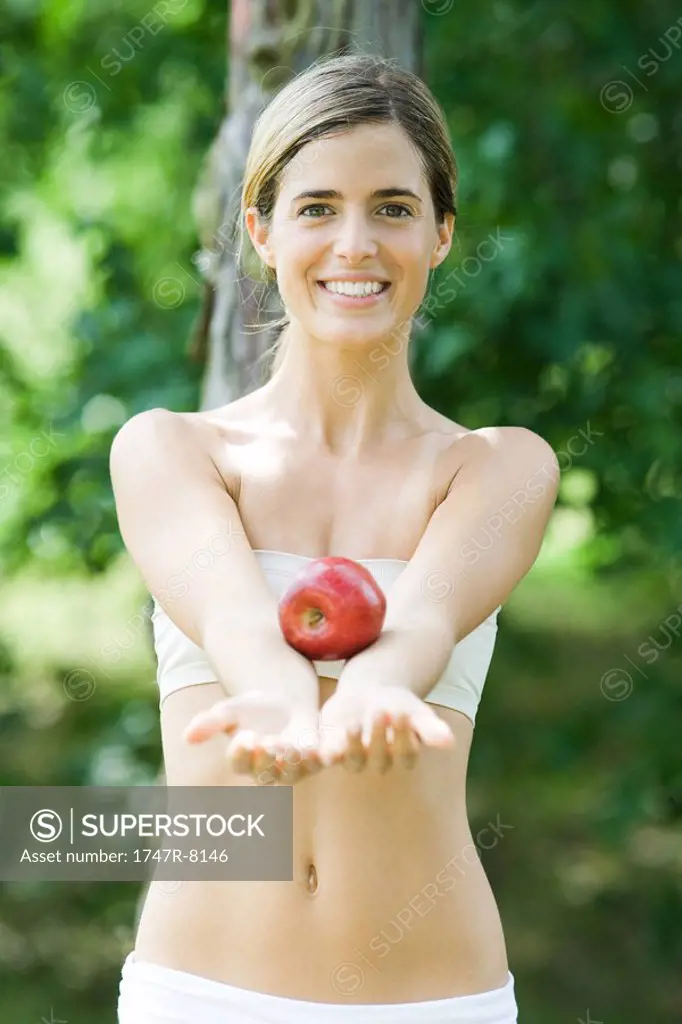 Young woman standing balancing apple on arms, smiling at camera