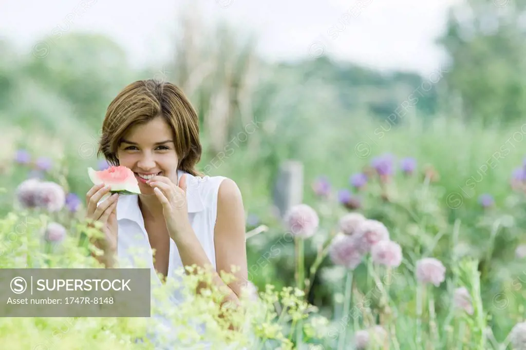 Young woman in garden, eating piece of watermelon