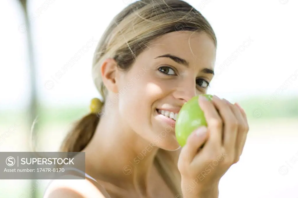 Woman holding up apple, glancing at camera