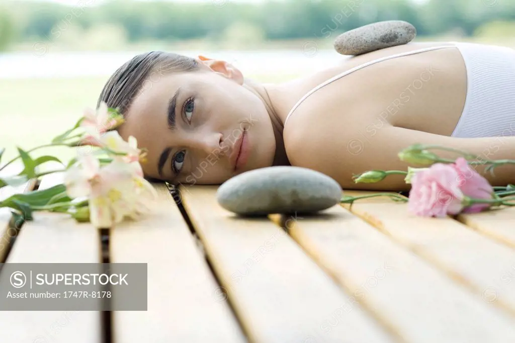 Woman lying on deck with hot stone on back surrounded by flowers and stones