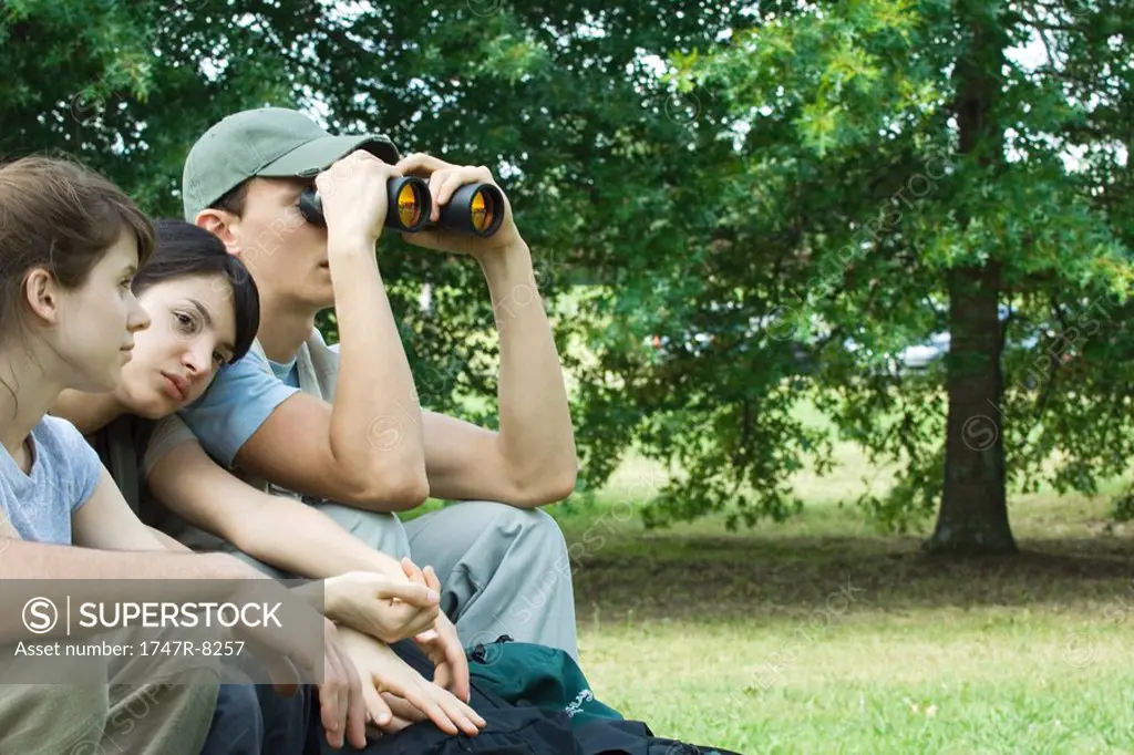 Young hikers sitting down, one looking through binoculars