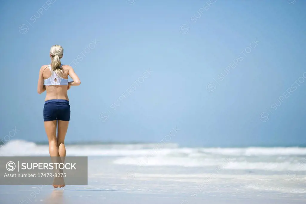 Young woman running on beach, rear view
