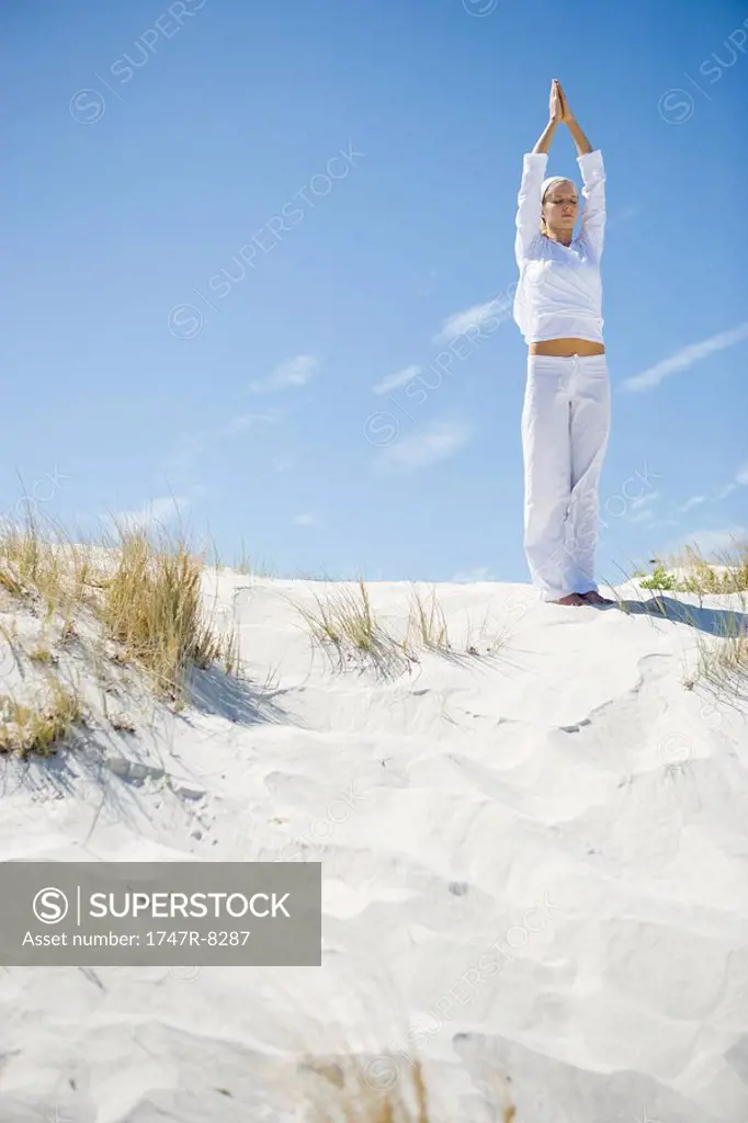 Young woman doing yoga on beach, full length