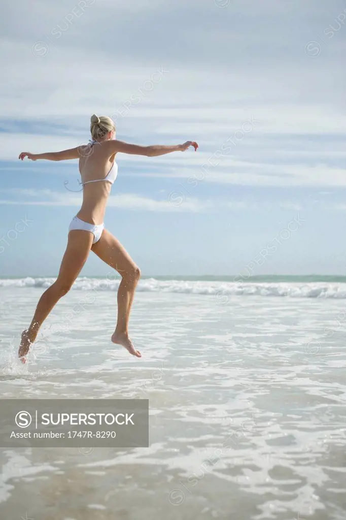 Young woman in bikini, leaping in surf