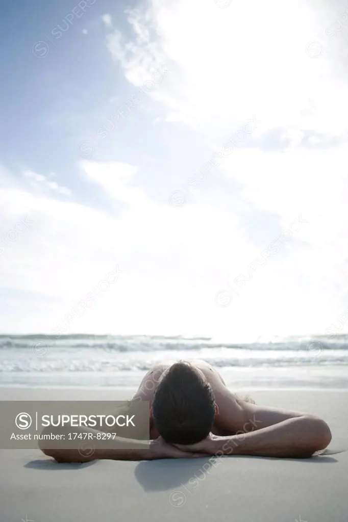 Young man lying on beach with hands behind head