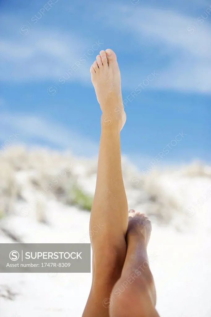 Young woman on beach, cropped view of legs in the air