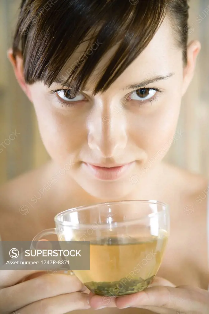 Young woman holding cup of herbal tea, looking at camera, close-up
