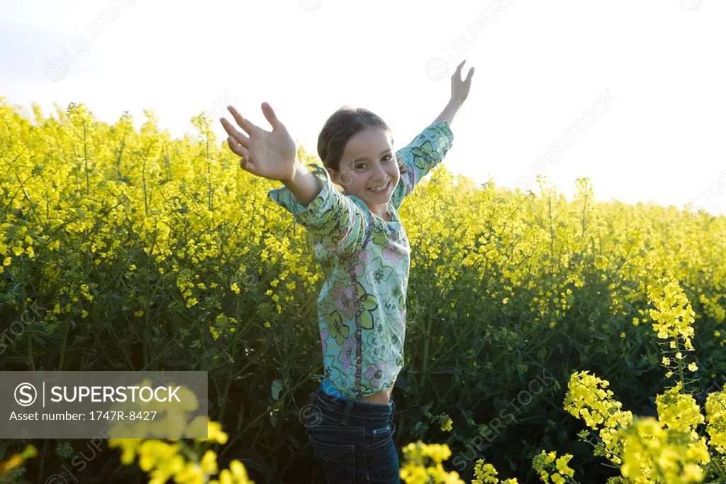 Girl standing in field with arms up, smiling at camera