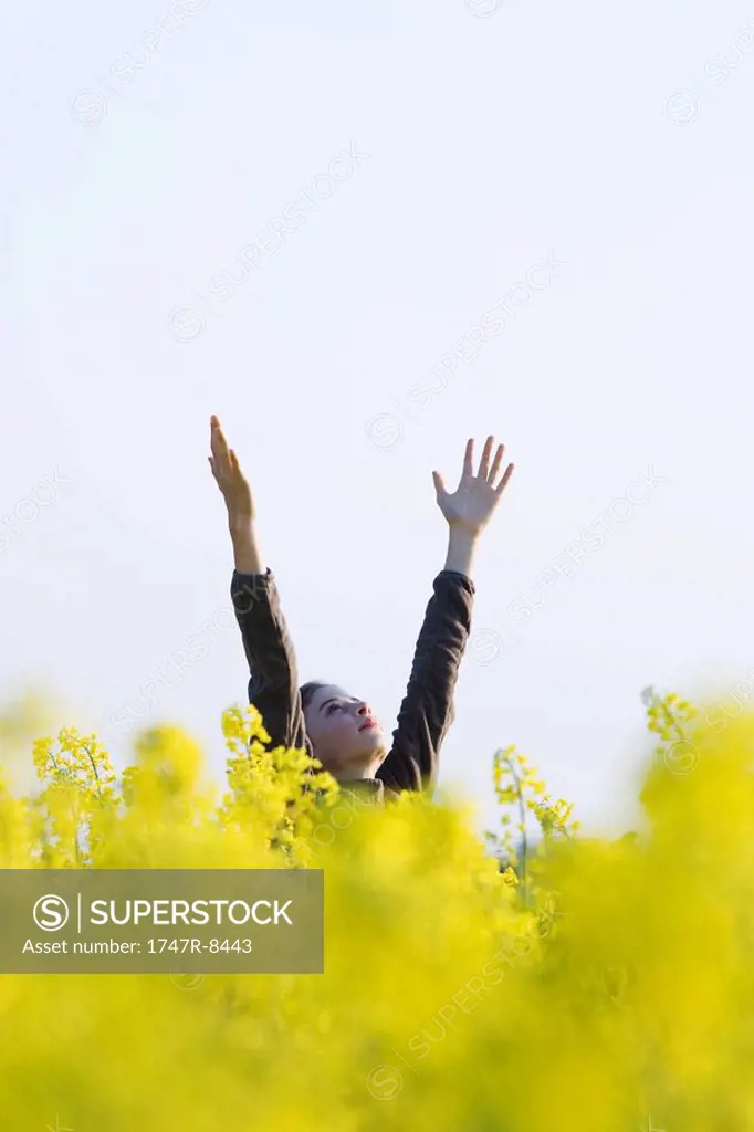 Girl standing in field with arms raised, looking up at sky