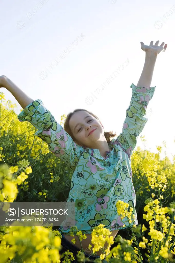 Girl standing in field of canola in bloom, arms raised, smiling