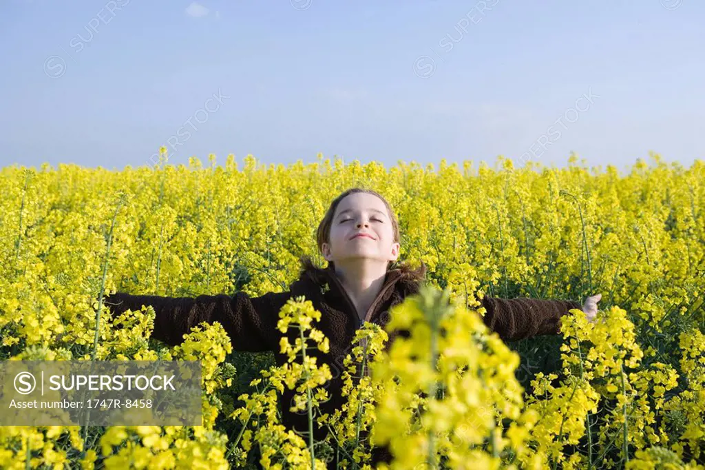 Girl standing in field of canola in bloom, head back and eyes closed