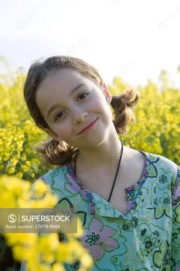 Girl standing in field of canola in bloom, smiling at camera, portrait
