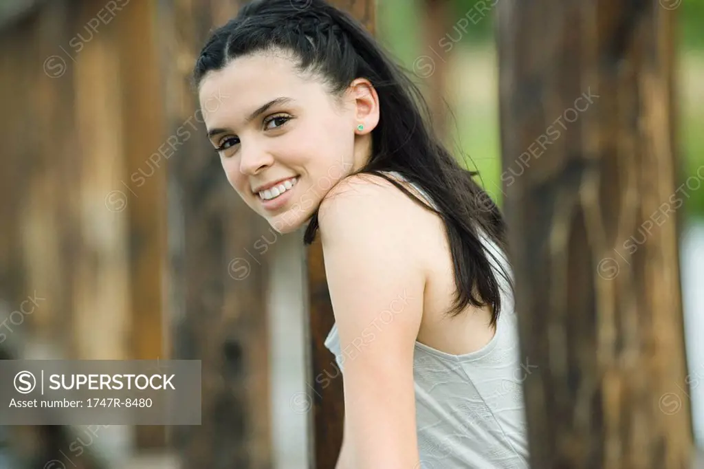 Teen girl standing in woods, smiling at camera
