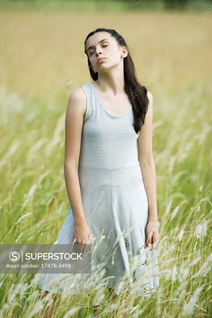 Teen girl standing in field with blade of grass in mouth, portrait