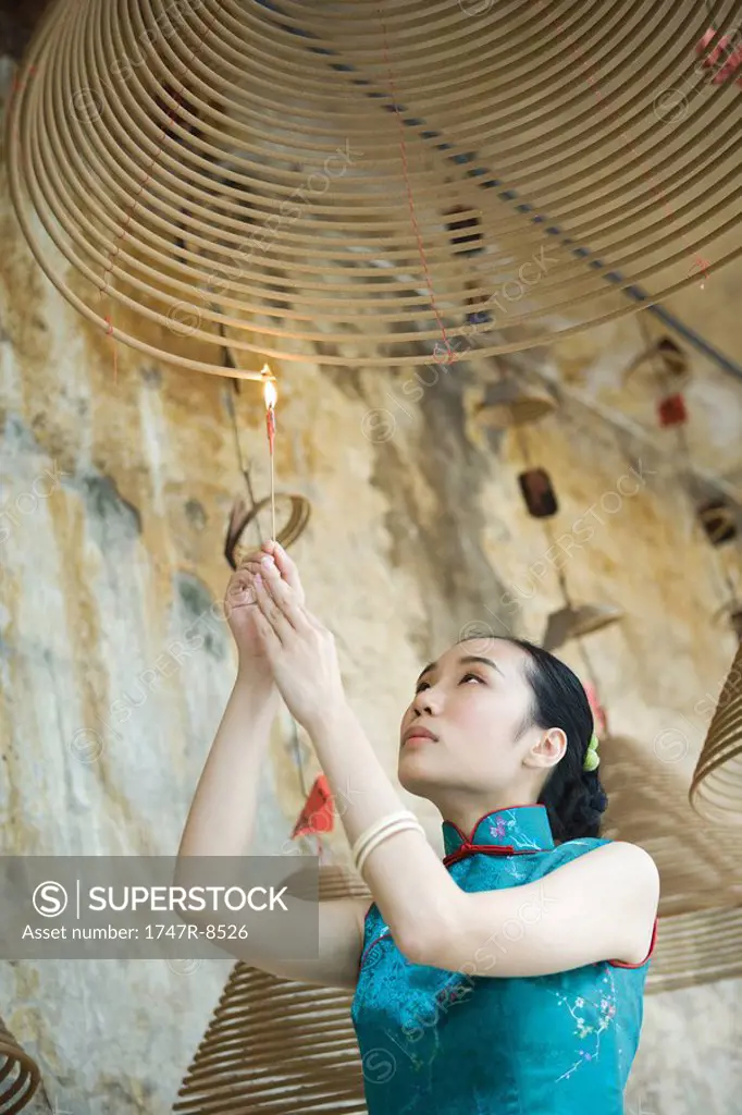 Young woman dressed in traditional Chinese clothing lighting spiral incense hanging from ceiling, low angle view
