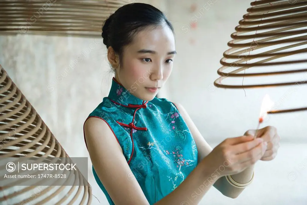 Young woman dressed in traditional Chinese clothing lighting spiral incense