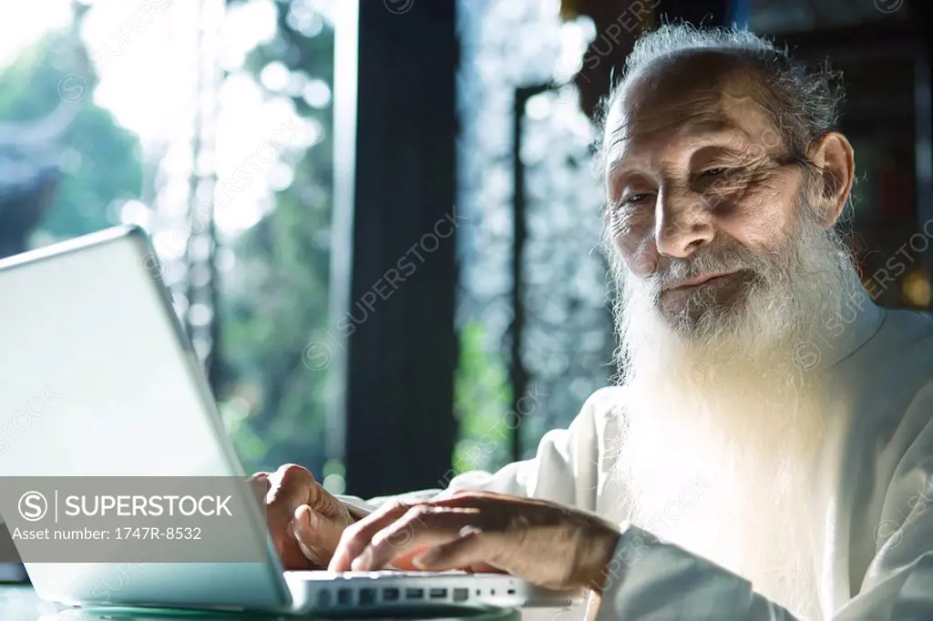 Elderly man in traditional Chinese clothing using laptop computer