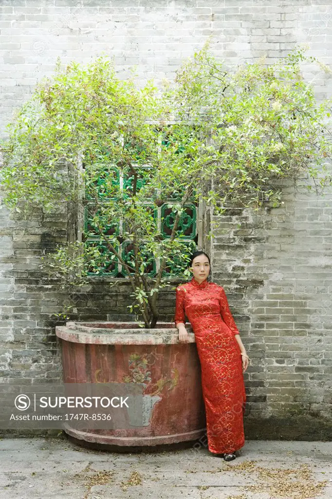 Young woman dressed in traditional Chinese clothing, standing next to potted tree