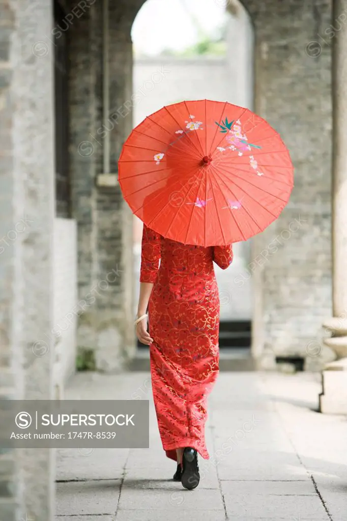Young woman dressed in traditional Chinese clothing walking with parasol, rear view