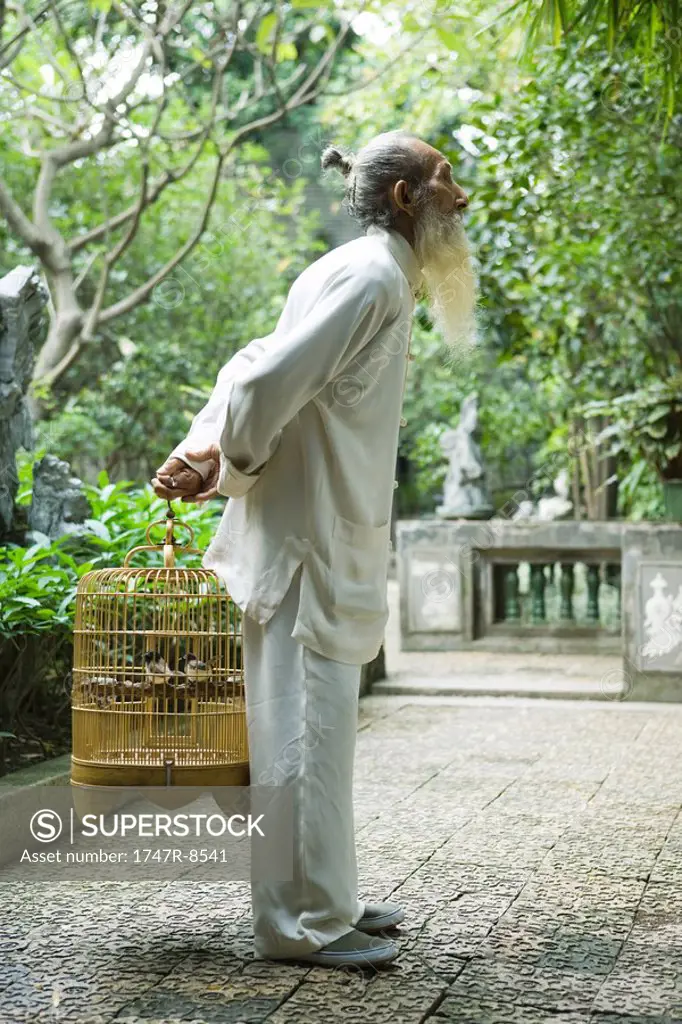 Elderly man in traditional Chinese clothing holding bird cage behind back