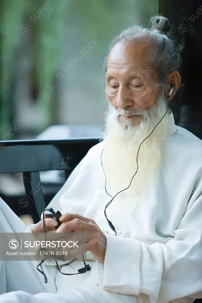 Elderly man in traditional Chinese clothing listening to MP3 player