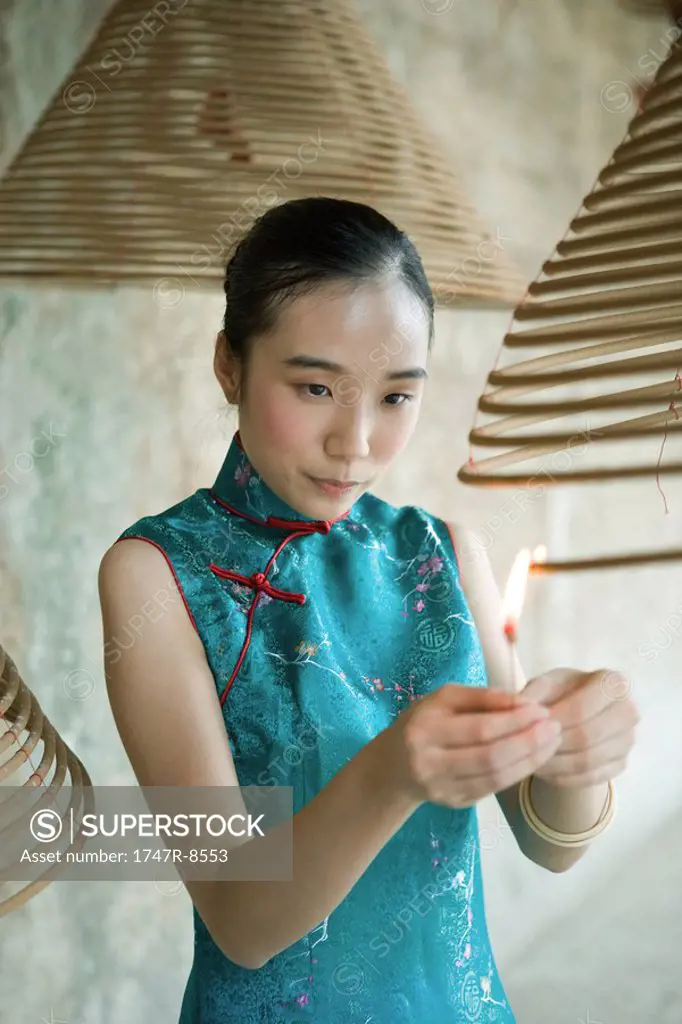Young woman dressed in traditional Chinese clothing lighting spiral incense hanging from ceiling