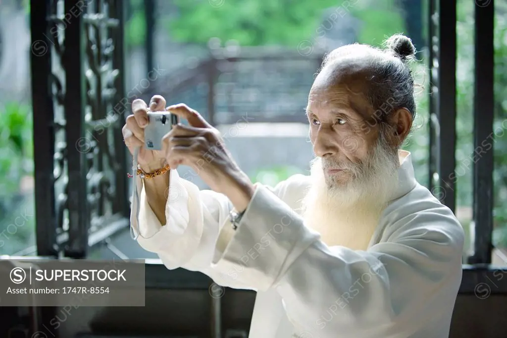 Elderly man in traditional Chinese clothing taking photo with digital camera