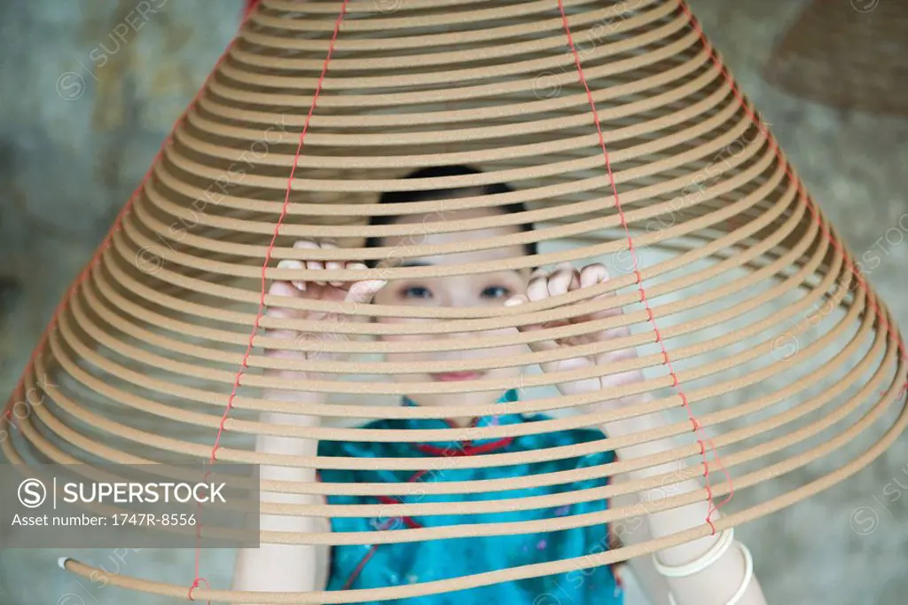 Young woman dressed in traditional Chinese clothing, peaking through spiral incense