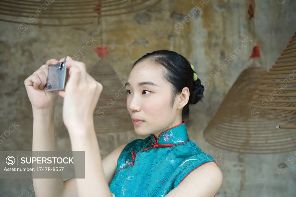 Young woman dressed in traditional Chinese clothing taking photo with digital camera