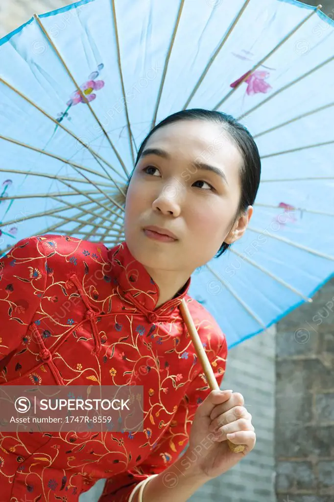 Young woman dressed in traditional Chinese clothing holding parasol over head