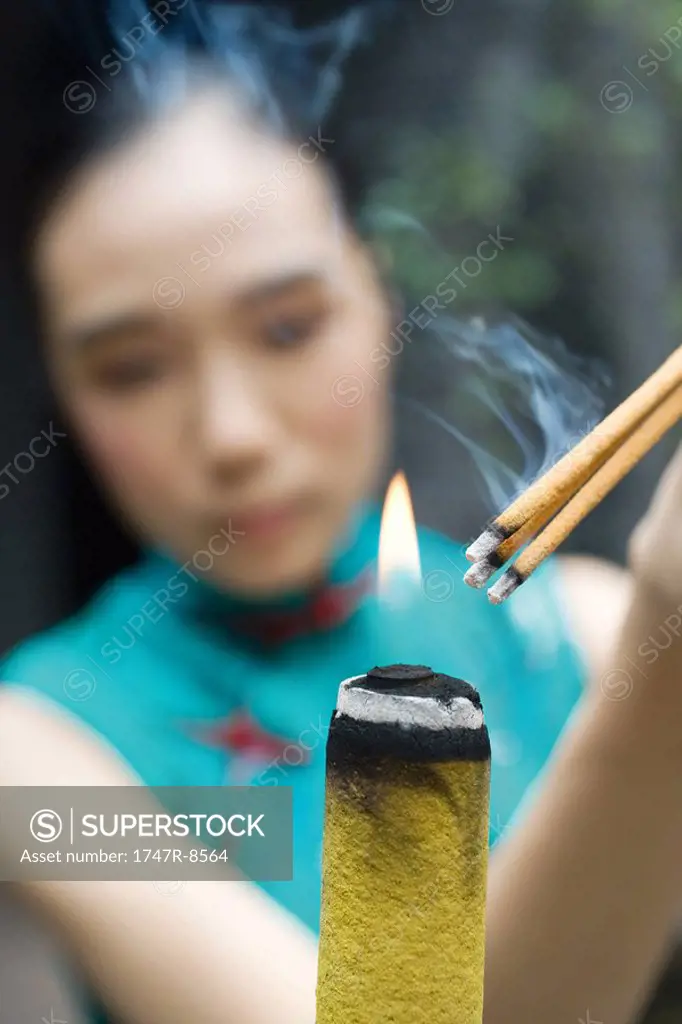 Young woman dressed in traditional Chinese clothing lighting sticks of incense
