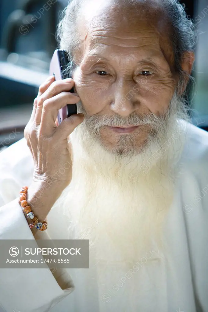 Elderly man in traditional Chinese clothing with long beard, using cell phone