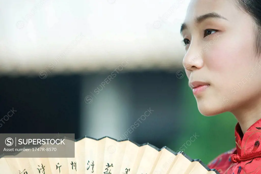 Young woman dressed in traditional Chinese clothing holding fan, cropped view